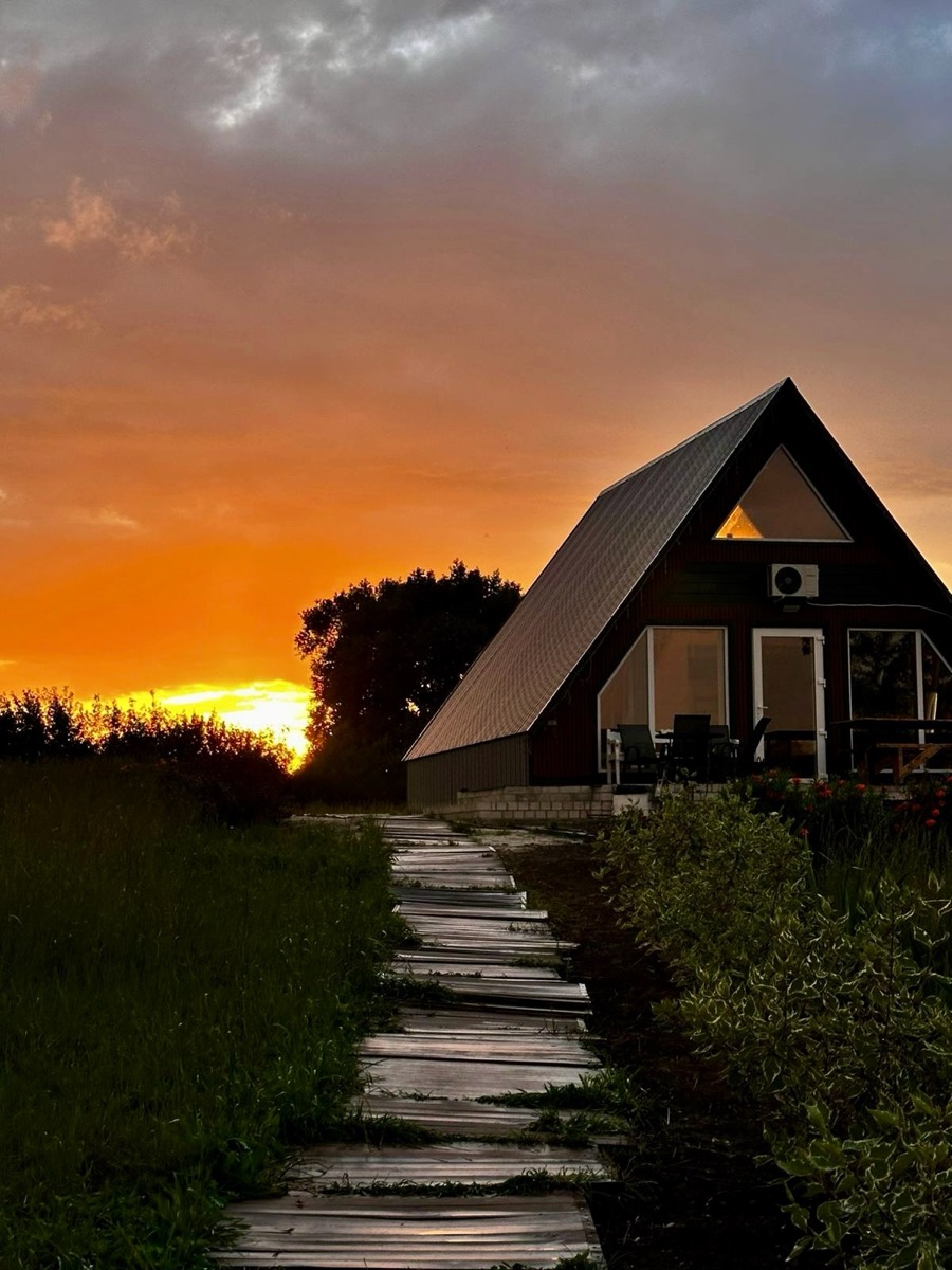 A-frame дом на закате, к нему ведёт деревянная дорожка